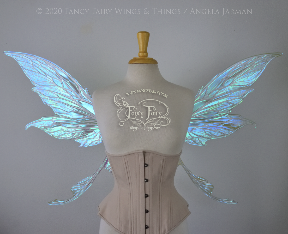 Front view of an ivory dress form wearing an alabaster underbust corset and large blue green iridescent fairy wings with white veins. Upper panels are elongated with pointed tips, curved ‘tail’, lots of thin vein detail