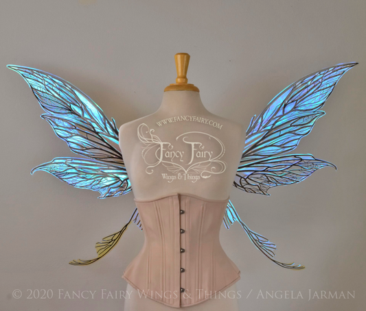 Front view of an ivory dress form wearing an alabaster underbust corset and large blue opal iridescent fairy wings with black veins. Upper panels are elongated with pointed tips, curved ‘tail’, lots of thin vein detail