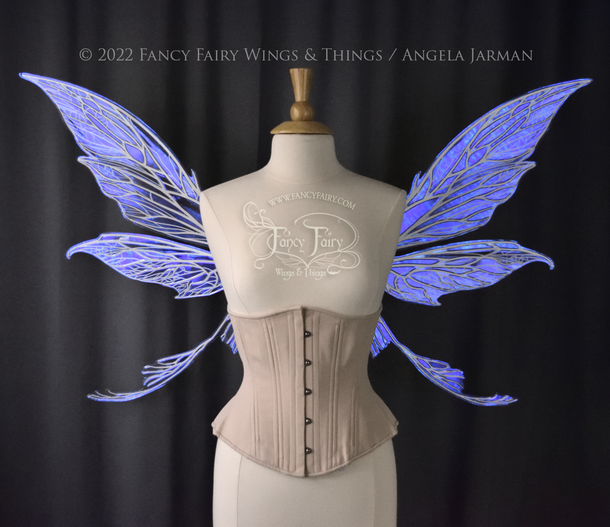 Front view of an ivory dress form wearing an alabaster underbust corset and large violet iridescent fairy wings with white veins. Upper panels are elongated with pointed tips, curved ‘tail’, lots of thin vein detail