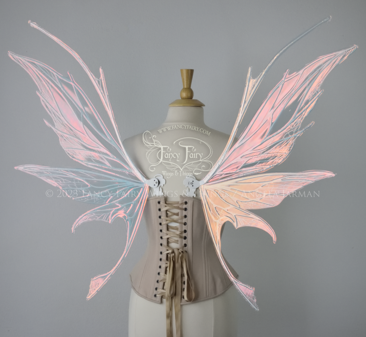 Back view of an ivory dress form wearing an alabaster underbust corset and large pink iridescent fairy wings with antennae on top. Upper panels come to a point, bottom panels have tails. Spikey, detailed white veins, plain white / grey background