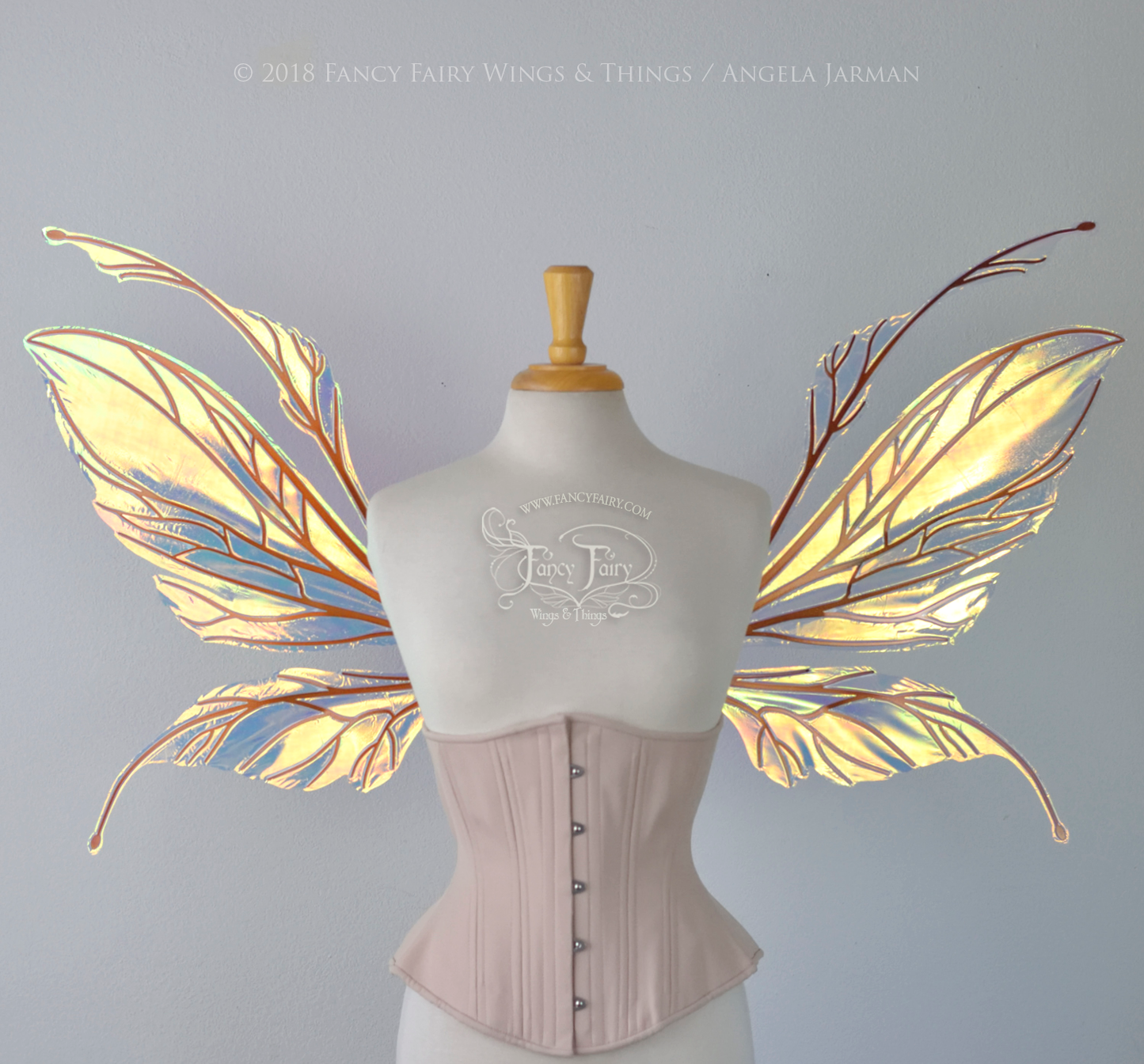 Large fairy wings featuring antennae along the top. The upper panels are elongated with semi-pointed tips, the lower panels are smaller with slender tips that curve downward. They are transparent iridescent with a yellow / orange / green shine with blue / pink undertones and the veins are metallic copper, worn on a dress form, front view