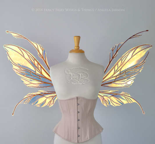 Large fairy wings featuring antennae along the top. The upper panels are elongated with semi-pointed tips, the lower panels are smaller with slender tips that curve downward. They are transparent iridescent with a yellow / orange / green shine with blue / pink undertones and the veins are metallic copper, worn on a dress form, front view