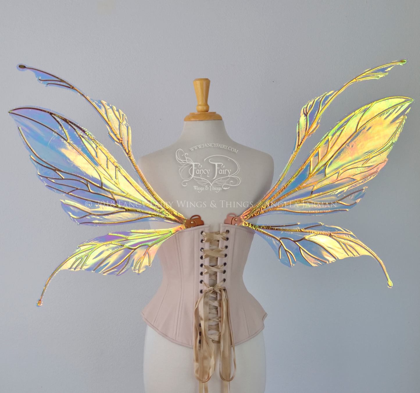 Large fairy wings featuring antennae along the top. The upper panels are elongated with semi-pointed tips, the lower panels are smaller with slender tips that curve downward. They are transparent iridescent with a yellow / orange / green shine with blue / pink undertones and the veins are metallic copper, worn on a dress form, back view
