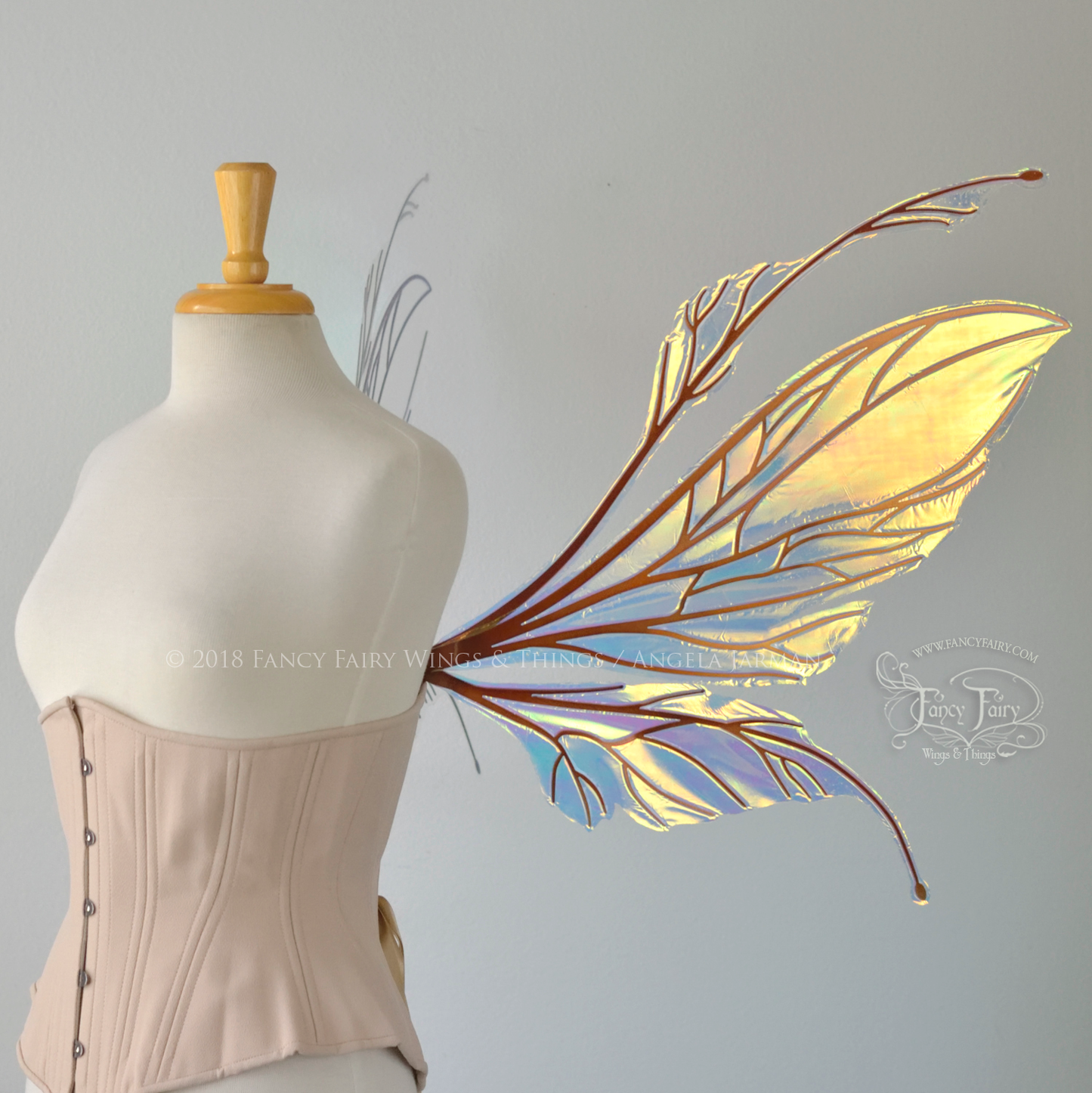 Large fairy wings featuring antennae along the top. The upper panels are elongated with semi-pointed tips, the lower panels are smaller with slender tips that curve downward. They are transparent iridescent with a yellow / orange / green shine with blue / pink undertones and the veins are metallic copper, worn on a dress form, right side view