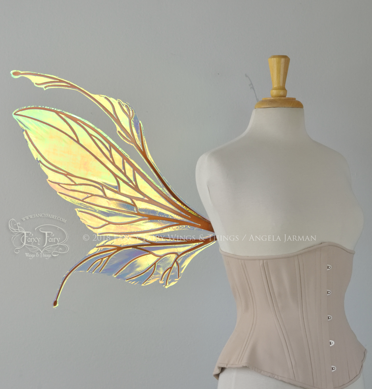 Large fairy wings featuring antennae along the top. The upper panels are elongated with semi-pointed tips, the lower panels are smaller with slender tips that curve downward. They are transparent iridescent with a yellow / orange / green shine with blue / pink undertones and the veins are metallic copper, worn on a dress form, left side view