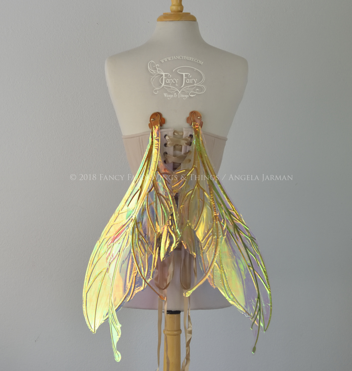 Large fairy wings featuring antennae along the top. The upper panels are elongated with semi-pointed tips, the lower panels are smaller with slender tips that curve downward. They are transparent iridescent with a yellow / orange / green shine with blue / pink undertones and the veins are metallic copper, worn on a dress form, back view, in resting position