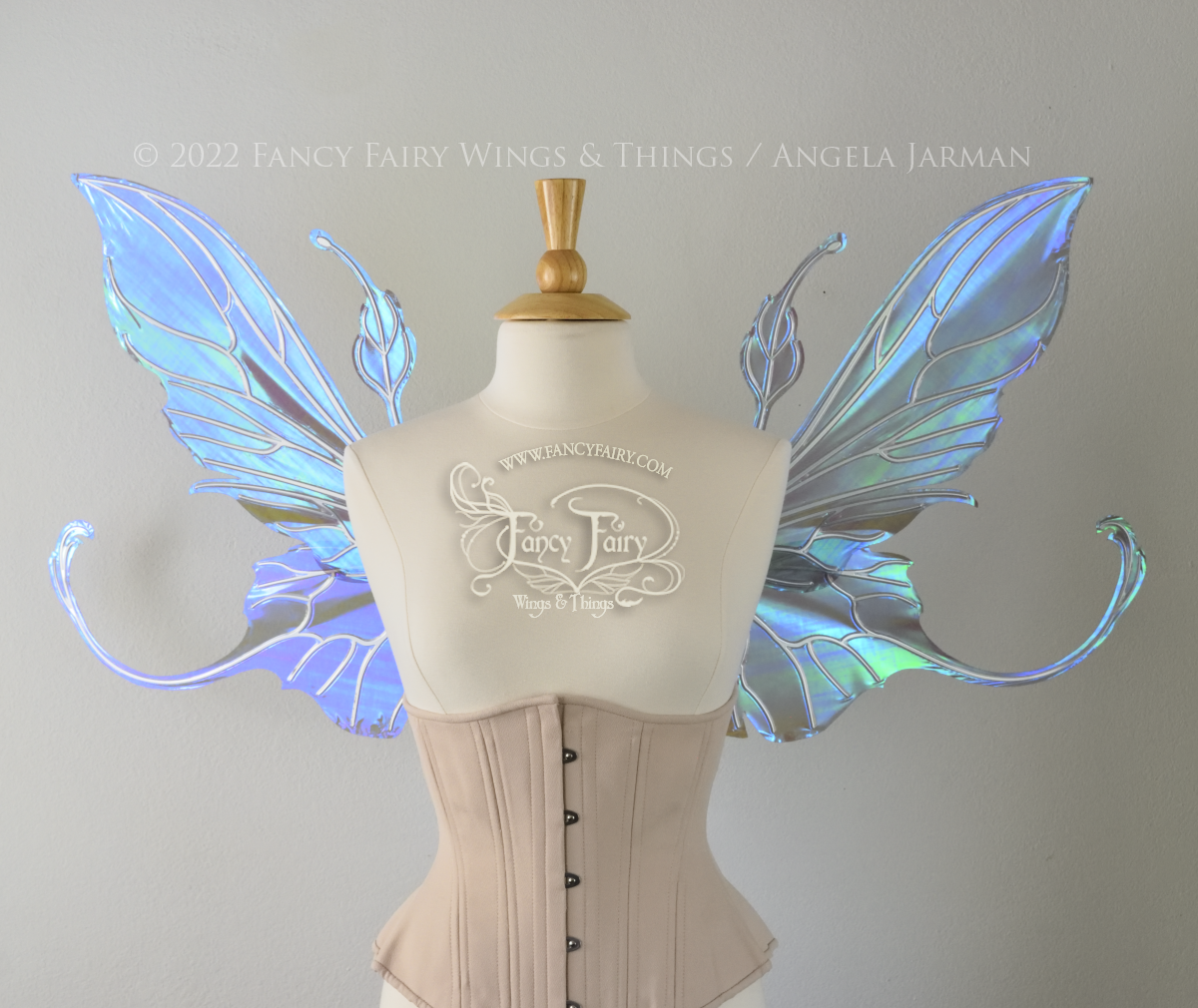 Front view of an ivory dress form wearing an alabaster underbust corset & large purple/blue iridescent fairy wings with elongated upper panels & antennae with bottom panels that have a tail curving upwards, silver veins