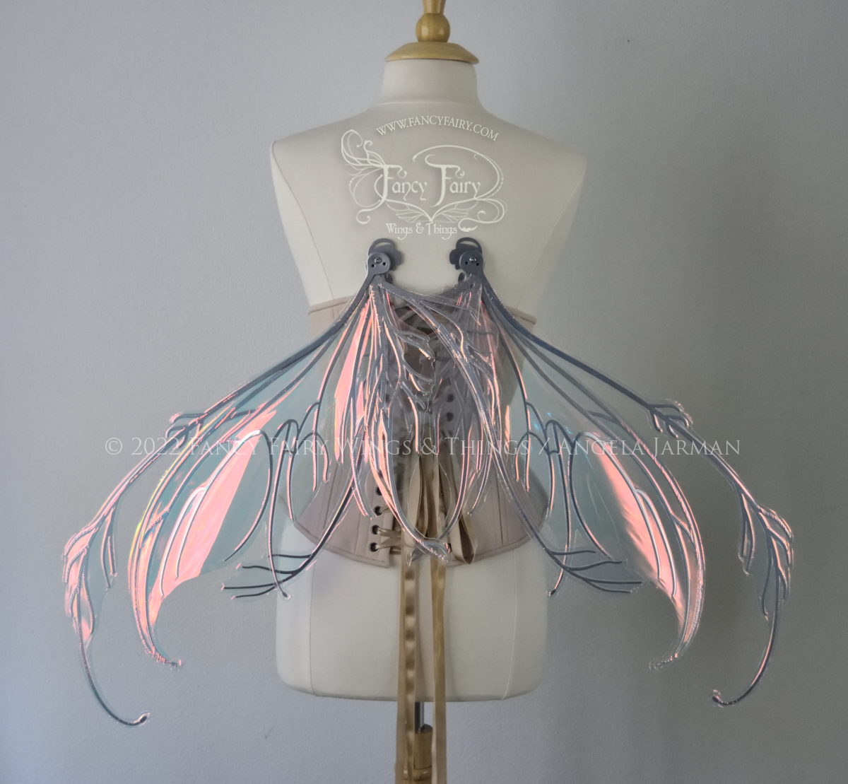 Back view of a dress form wearing an underbust corset & 'Fauna' transparent pink iridescent fairy wings with downward curved tips, antennae & wispy 'tails', with silver veining, in resting position