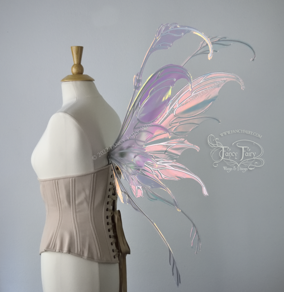 Back 3/4 side view of a dress form wearing an underbust corset & 'Fauna' transparent pink iridescent fairy wings with downward curved tips, antennae & wispy 'tails', with silver veining