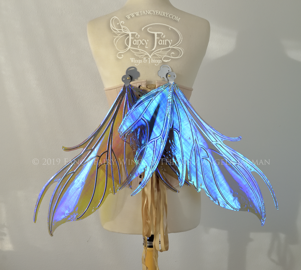 Back view of a dress form wearing an underbust corset & purple / blue iridescent fairy wings with a spikey shape, with silver veins, in resting position