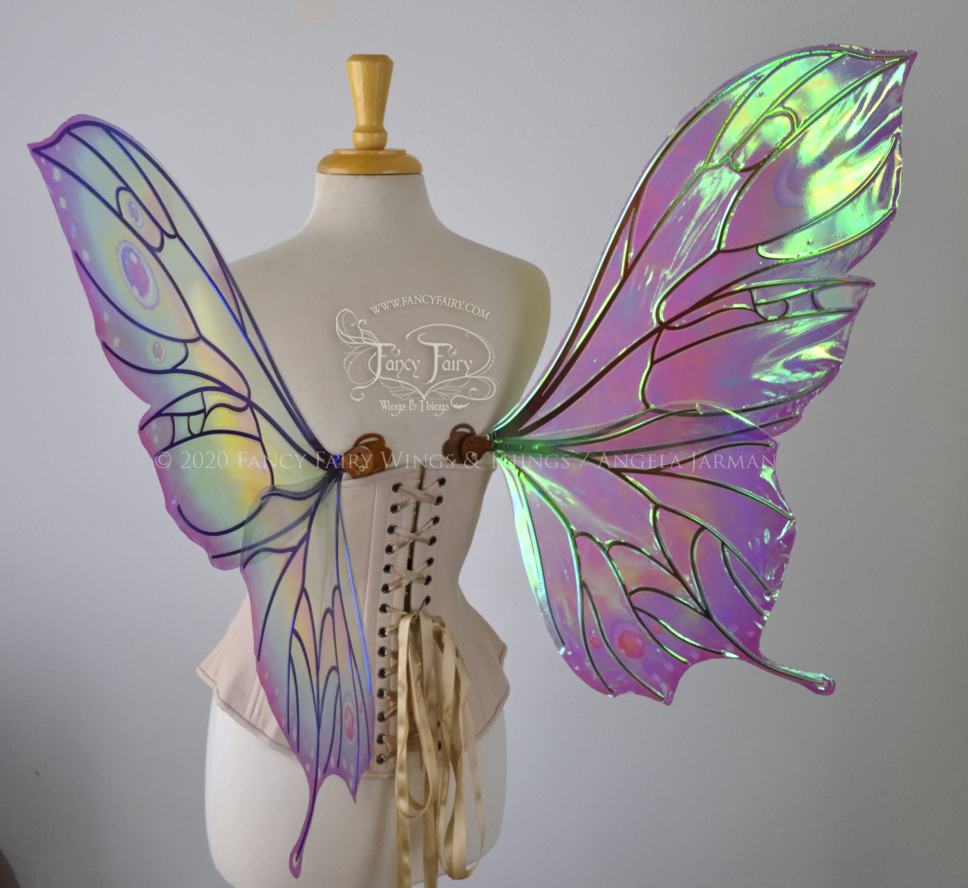 Bright rainbow colored iridescent fairy wings in a butterfly sort of shape with small 'tails' on the bottom panels curving slightly up, with copper veins. Worn on a dress form, back 3/4 view