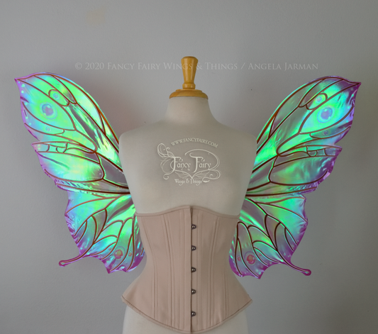 Bright rainbow colored iridescent fairy wings in a butterfly sort of shape with small 'tails' on the bottom panels curving slightly up, with copper veins. Worn on a dress form, front view