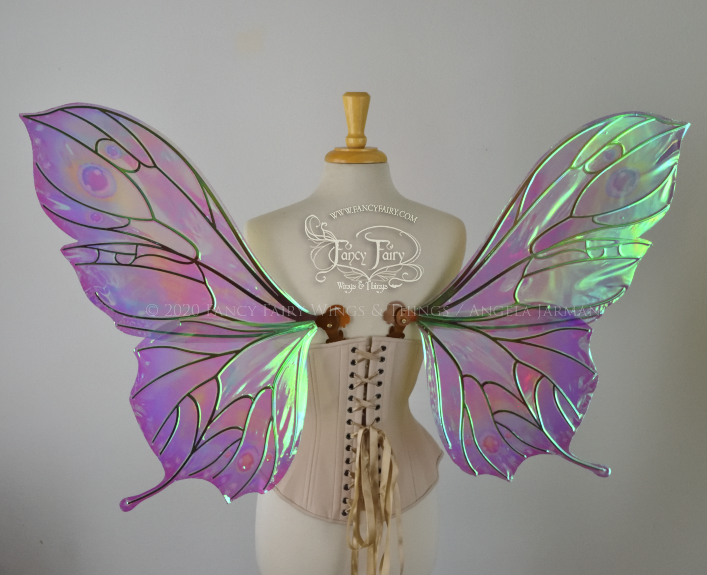 Bright rainbow colored iridescent fairy wings in a butterfly sort of shape with small 'tails' on the bottom panels curving slightly up, with copper veins. Worn on a dress form, back view