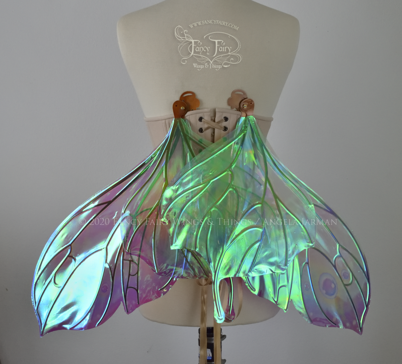 Bright rainbow colored iridescent fairy wings in a butterfly sort of shape with small 'tails' on the bottom panels curving slightly up, with copper veins. Worn on a dress form, back view, in resting position