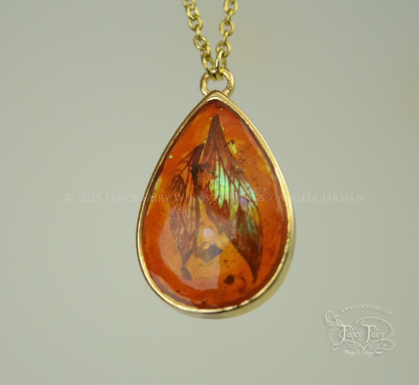 Closeup of faux amber pendant with iridescent fairy wings trapped inside, hanging by gold plated chain