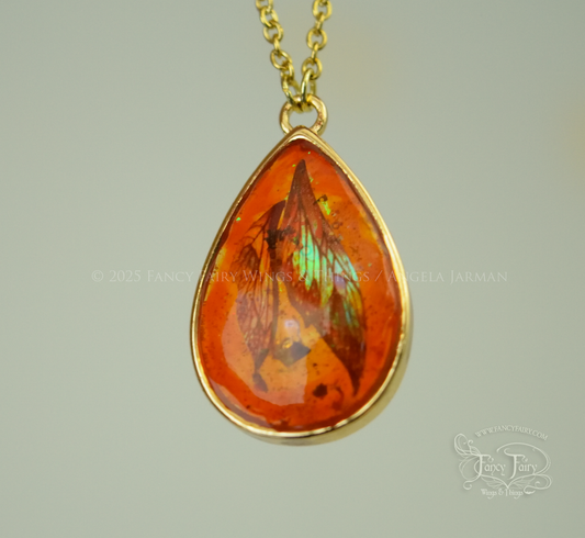 Closeup of faux amber pendant with iridescent fairy wings trapped inside, hanging by gold plated chain