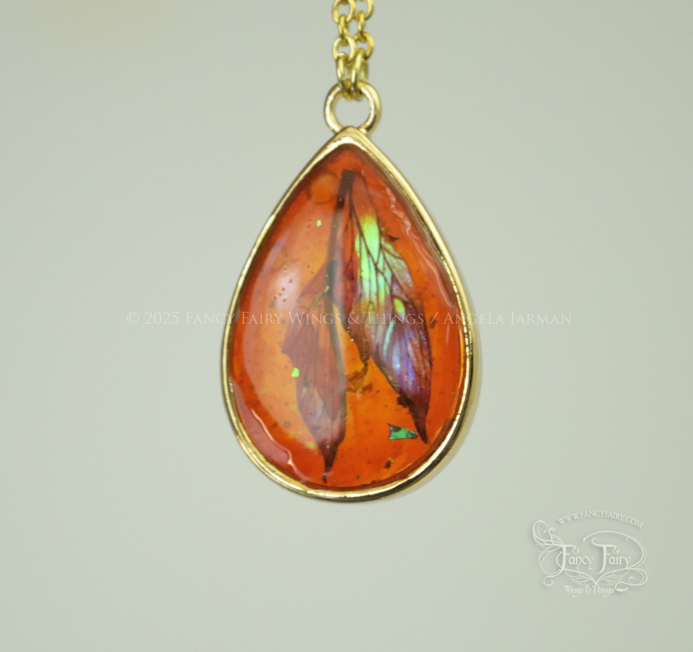 Closeup of faux amber pendant with iridescent fairy wings trapped inside, hanging by gold plated chain