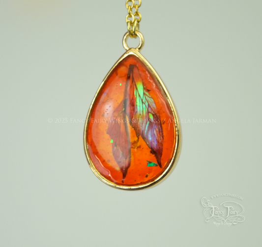 Closeup of faux amber pendant with iridescent fairy wings trapped inside, hanging by gold plated chain