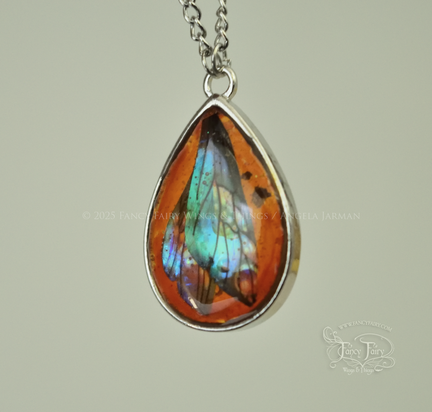 Closeup of faux amber pendant with teal iridescent fairy wings trapped inside, hanging by silver plated chain