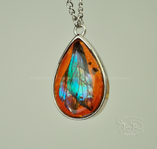 Closeup of faux amber pendant with teal iridescent fairy wings trapped inside, hanging by silver plated chain