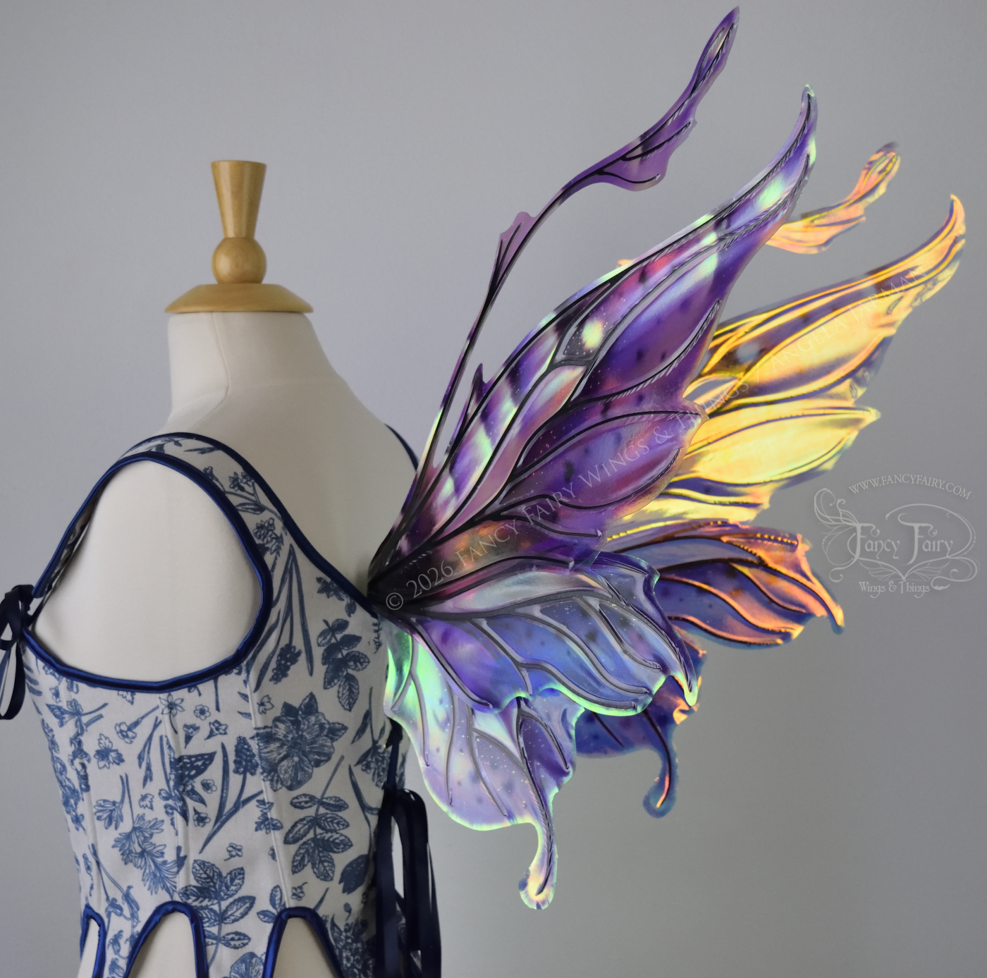 Iridescent fairy wings in purple, pink, teal and black have wavy antennae & upward curving tips, worn on a dress form, back 3/4 view