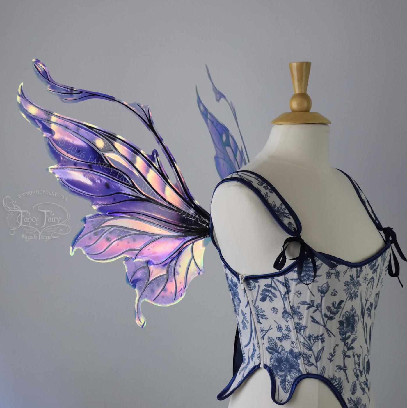 Iridescent fairy wings in purple, pink, teal and black have wavy antennae & upward curving tips, worn on a dress form, left side view
