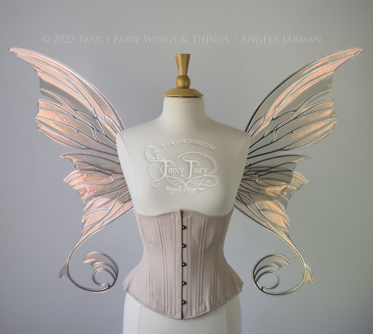 Front view of an ivory dress form wearing an alabaster underbust corset and large rose gold iridescent fairy wings with lots of intricate silver veins, some have 'thorns'. Upper panels curve slightly downwards along top edge with pointy tips, bottom panels have tails