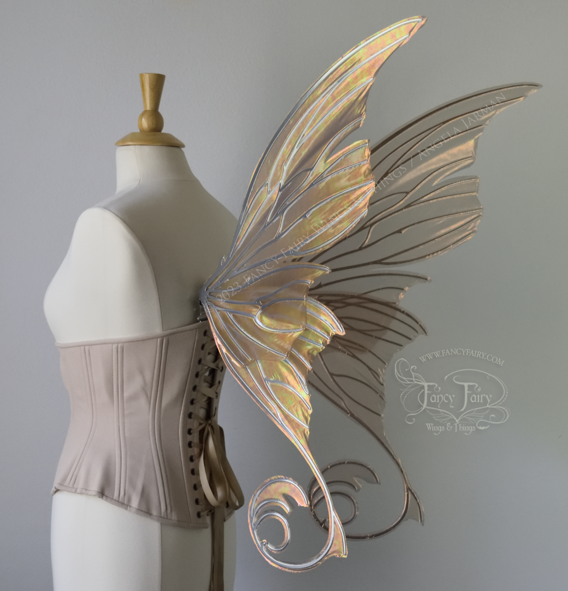 Back 3/4 view of an ivory dress form wearing an alabaster underbust corset and large rose gold iridescent fairy wings with lots of intricate silver veins, some have 'thorns'. Upper panels curve slightly downwards along top edge with pointy tips, bottom panels have tails