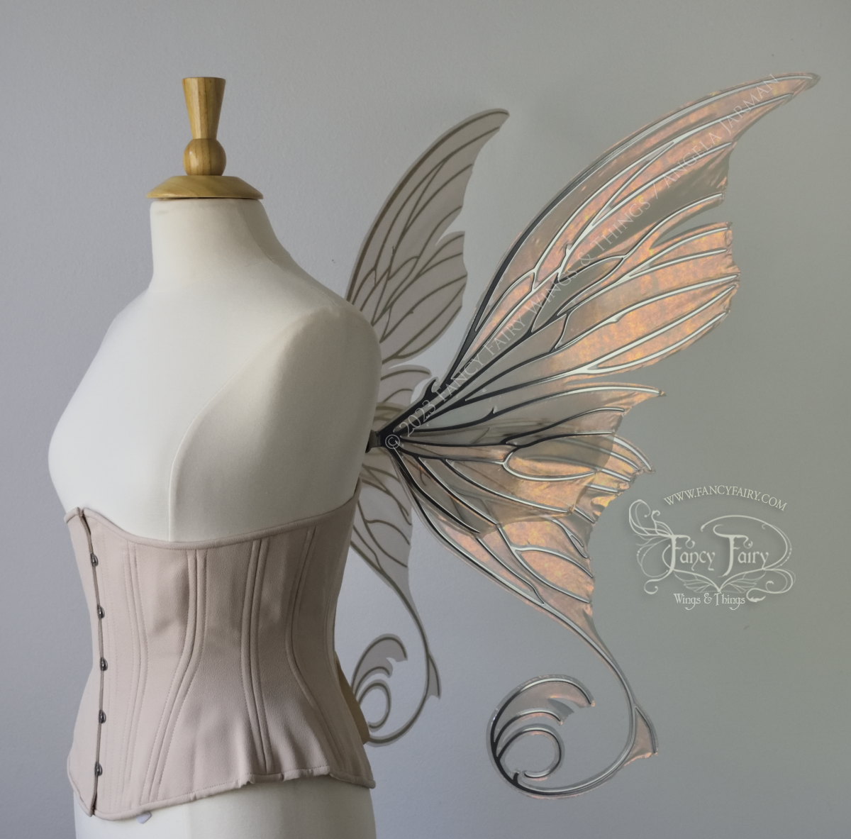 Right side view of an ivory dress form wearing an alabaster underbust corset and large rose gold iridescent fairy wings with lots of intricate silver veins, some have 'thorns'. Upper panels curve slightly downwards along top edge with pointy tips, bottom panels have tails