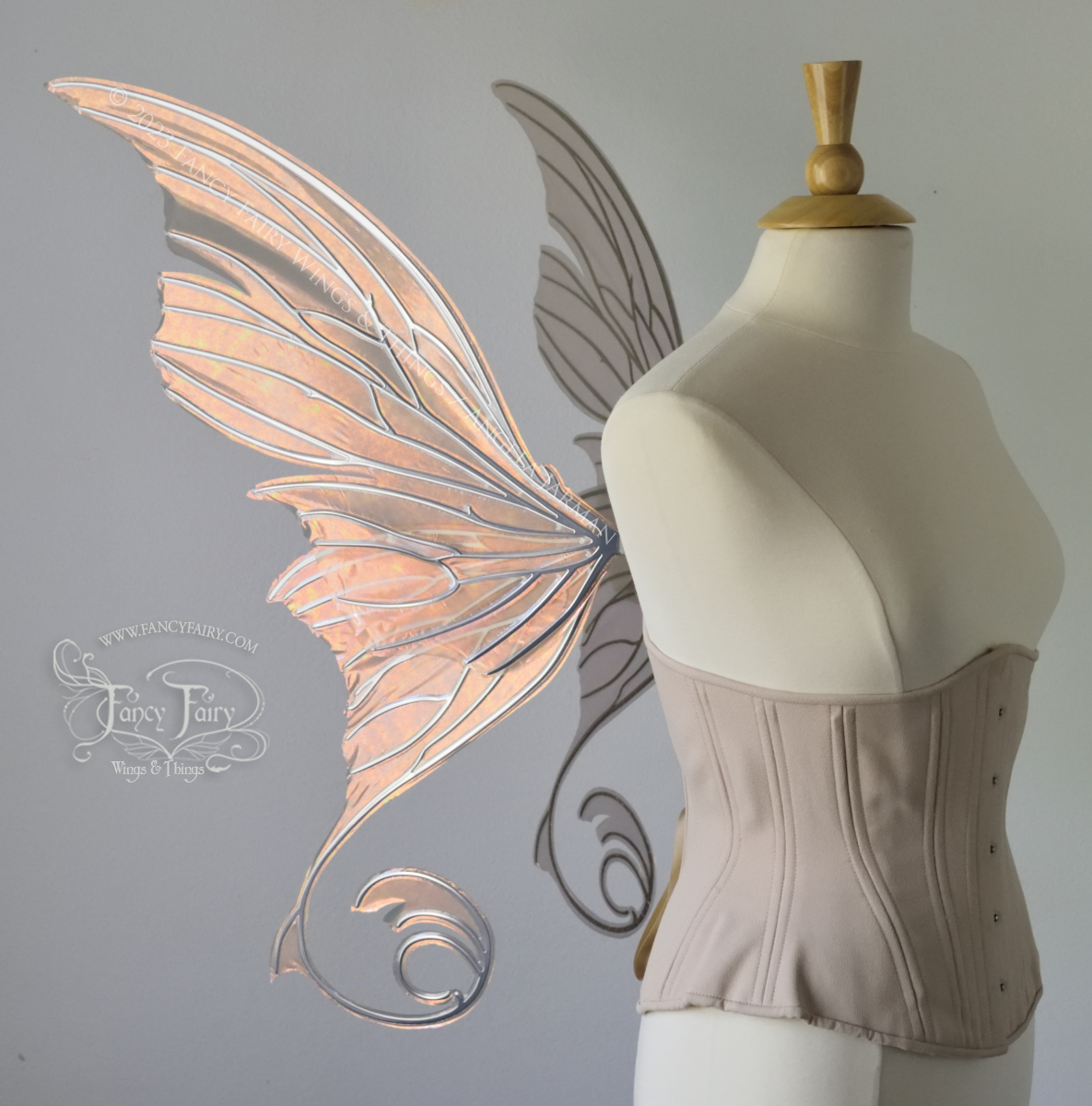 Left side view of an ivory dress form wearing an alabaster underbust corset and large rose gold iridescent fairy wings with lots of intricate silver veins, some have 'thorns'. Upper panels curve slightly downwards along top edge with pointy tips, bottom panels have tails