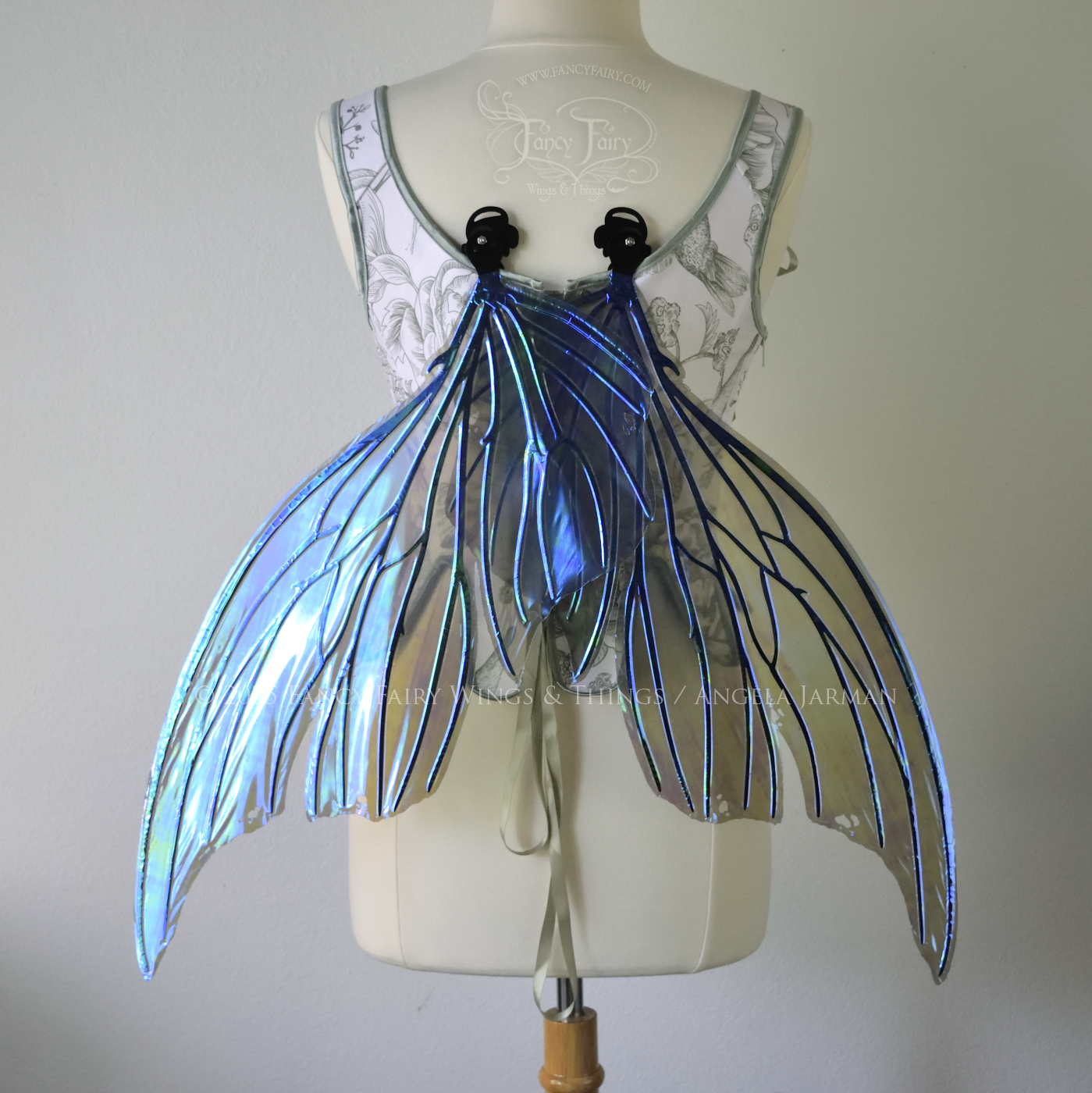 Back view of an ivory dress form wearing large violet iridescent fairy wings with lots of intricate black veins, some have 'thorns', in resting position