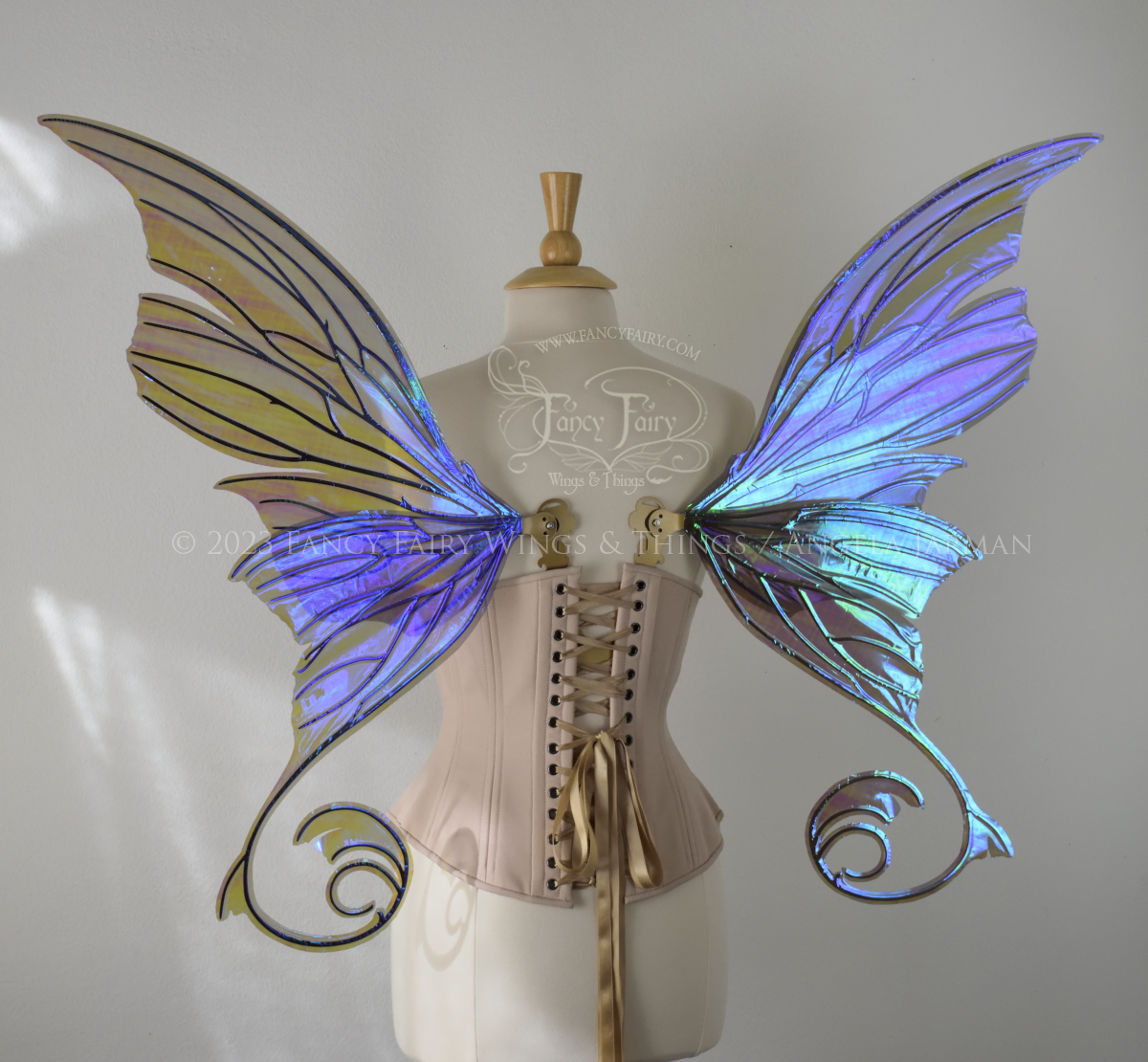 Back view of an ivory dress form wearing an alabaster underbust corset and large purple iridescent fairy wings with lots of intricate gold veins, some have 'thorns'. Upper panels curve slightly downwards along top edge with pointy tips, bottom panels have tails