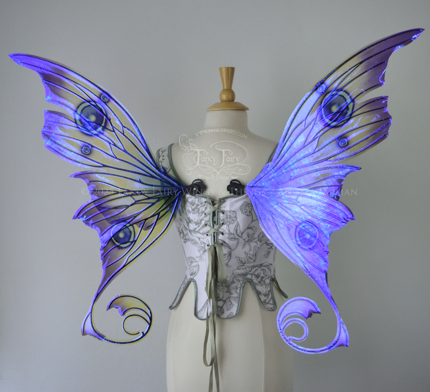Large purple, teal & green iridescent fairy wings with thorny black veins The upper panels curve slightly downwards along the top edge with pointy tips, the bottom panels have tails that curve inward toward the body. Worn on a dress form, back view