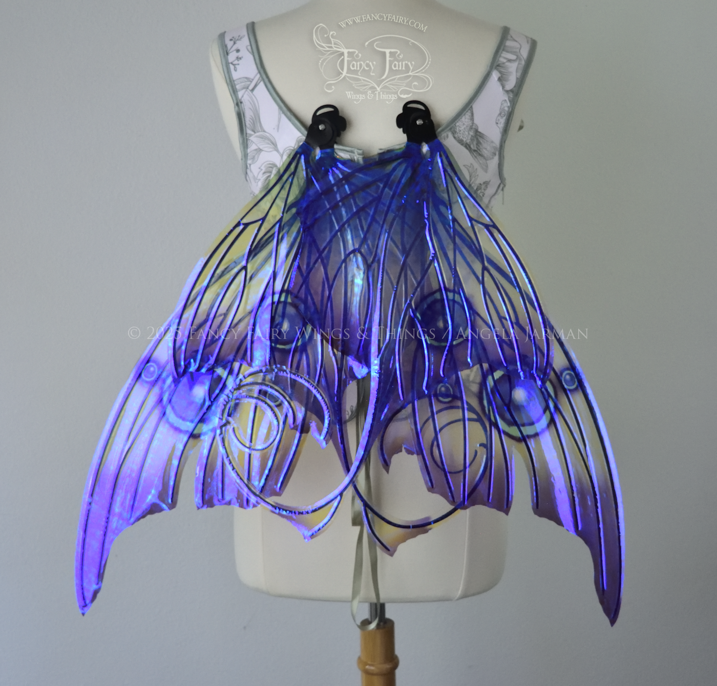 Large purple, teal & green iridescent fairy wings with thorny black veins The upper panels curve slightly downwards along the top edge with pointy tips, the bottom panels have tails that curve inward toward the body. Worn on a dress form, back view, in resting position