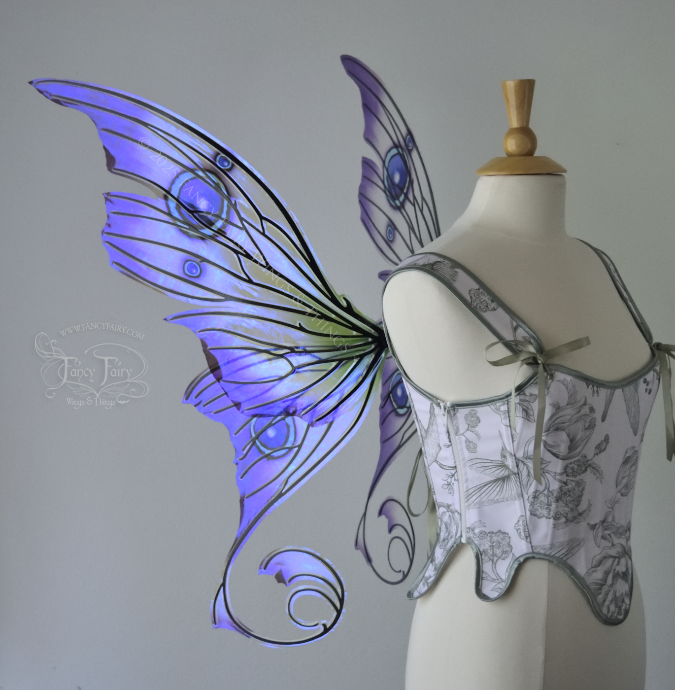 Large purple, teal & green iridescent fairy wings with thorny black veins The upper panels curve slightly downwards along the top edge with pointy tips, the bottom panels have tails that curve inward toward the body. Worn on a dress form, left side view