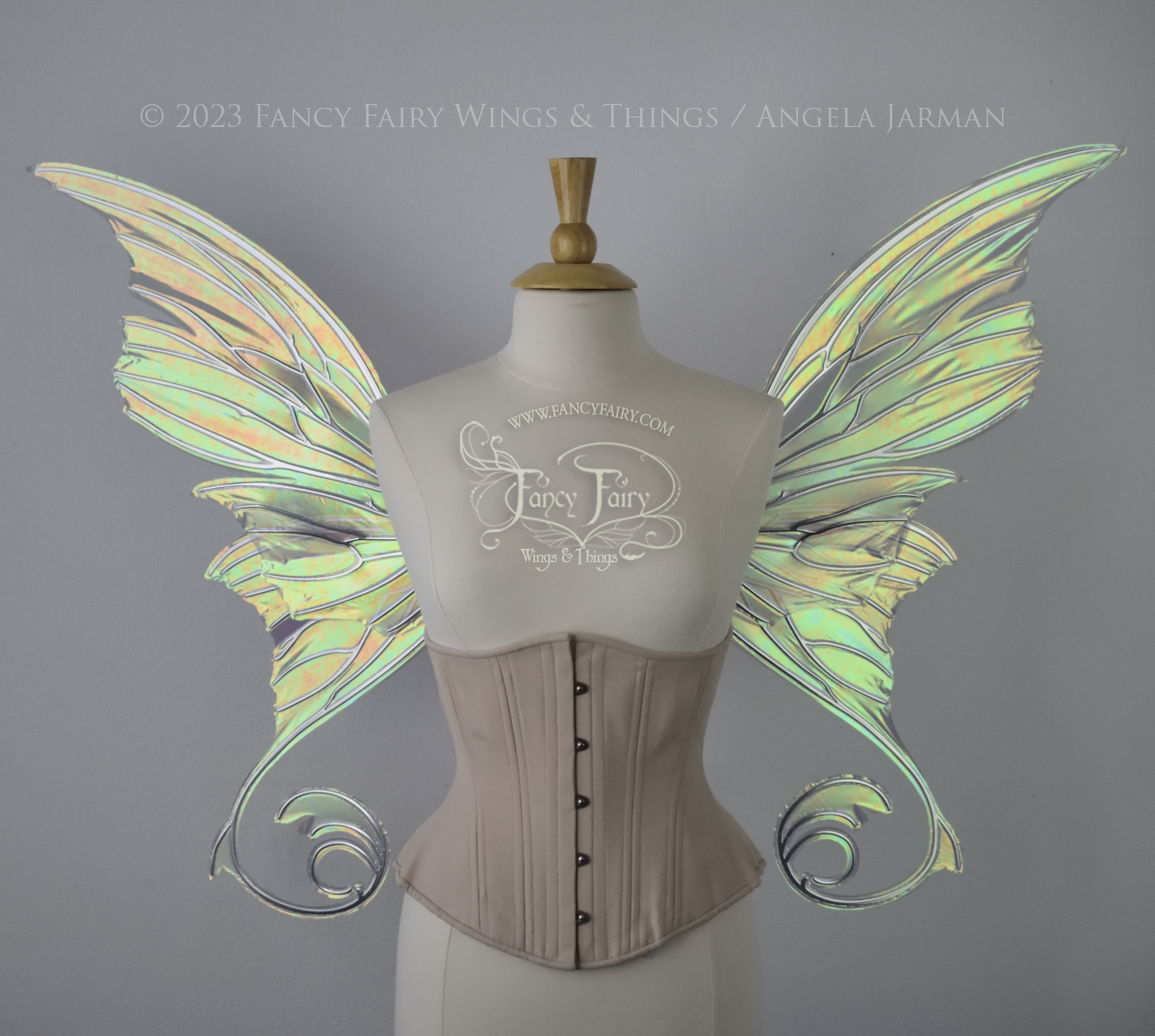 Front view of an ivory dress form wearing an alabaster underbust corset and large patina green iridescent fairy wings with lots of intricate silver veins, some have 'thorns'. Upper panels curve slightly downwards along top edge with pointy tips, bottom panels have tails