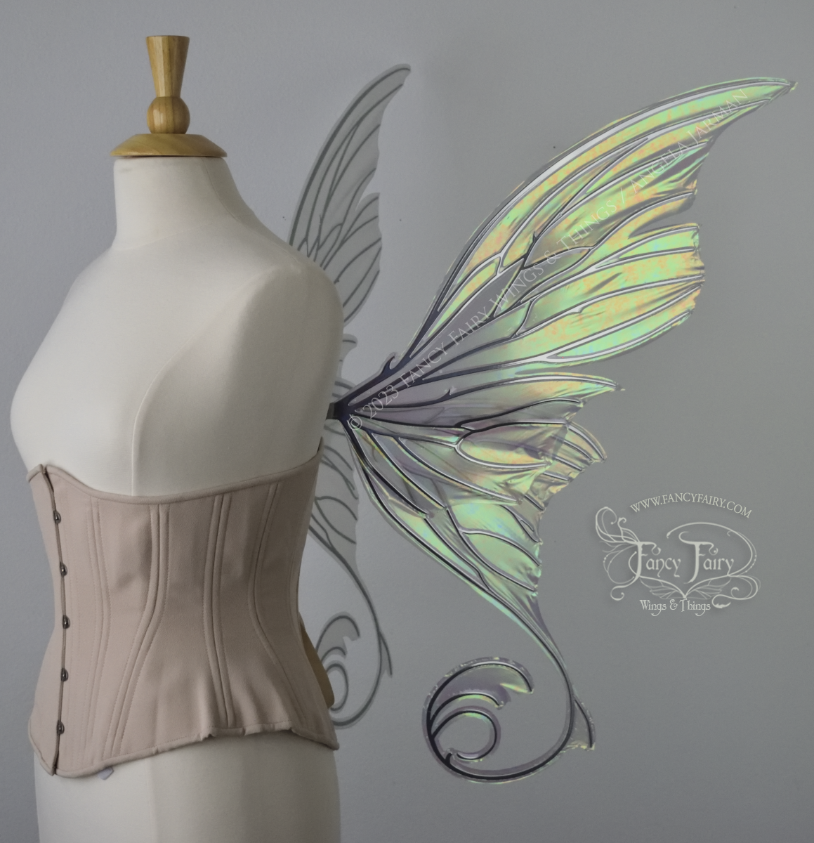 Right side view of an ivory dress form wearing an alabaster underbust corset and large rose gold iridescent fairy wings with lots of intricate silver veins, some have 'thorns'. Upper panels curve slightly downwards along top edge with pointy tips, bottom panels have tails