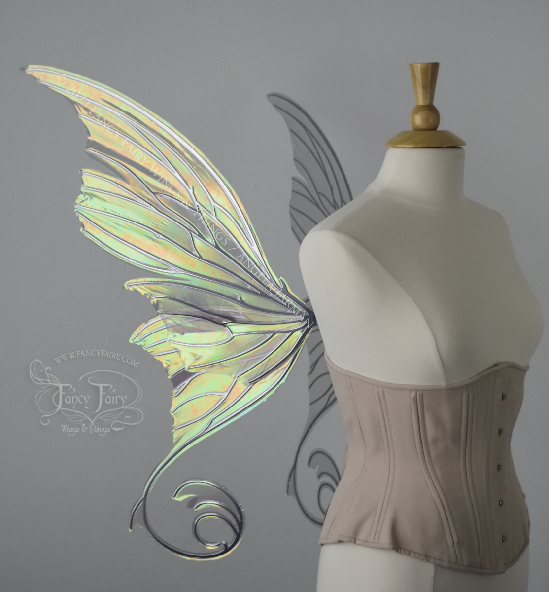 Left side view of an ivory dress form wearing an alabaster underbust corset and large rose gold iridescent fairy wings with lots of intricate silver veins, some have 'thorns'. Upper panels curve slightly downwards along top edge with pointy tips, bottom panels have tails