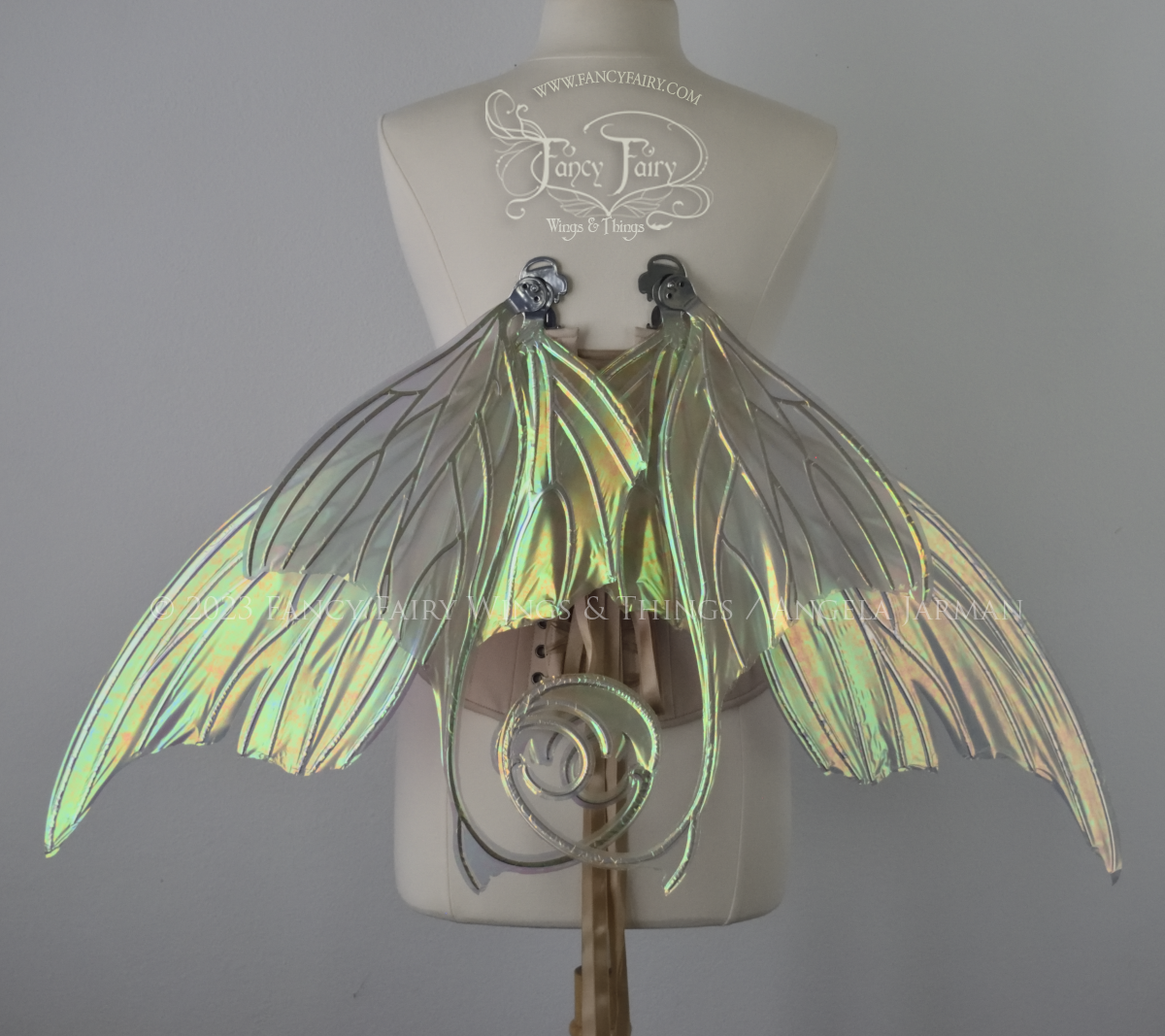 Back view of an ivory dress form wearing an alabaster underbust corset and large rose gold iridescent fairy wings with lots of intricate silver veins, some have 'thorns'. Upper panels curve slightly downwards along top edge with pointy tips, bottom panels have tails, in resting position