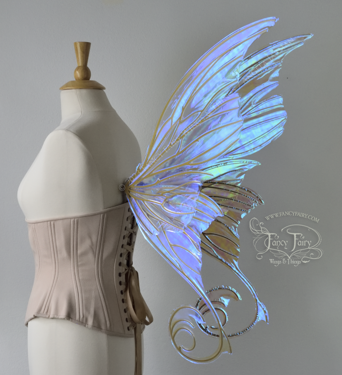Back 3/4 view of a dress form wearing an underbust corset & large blue iridescent fairy wings with lots of intricate veins, some have 'thorns'. Upper panels curve slightly downwards along top edge with pointy tips, bottom panels have tails