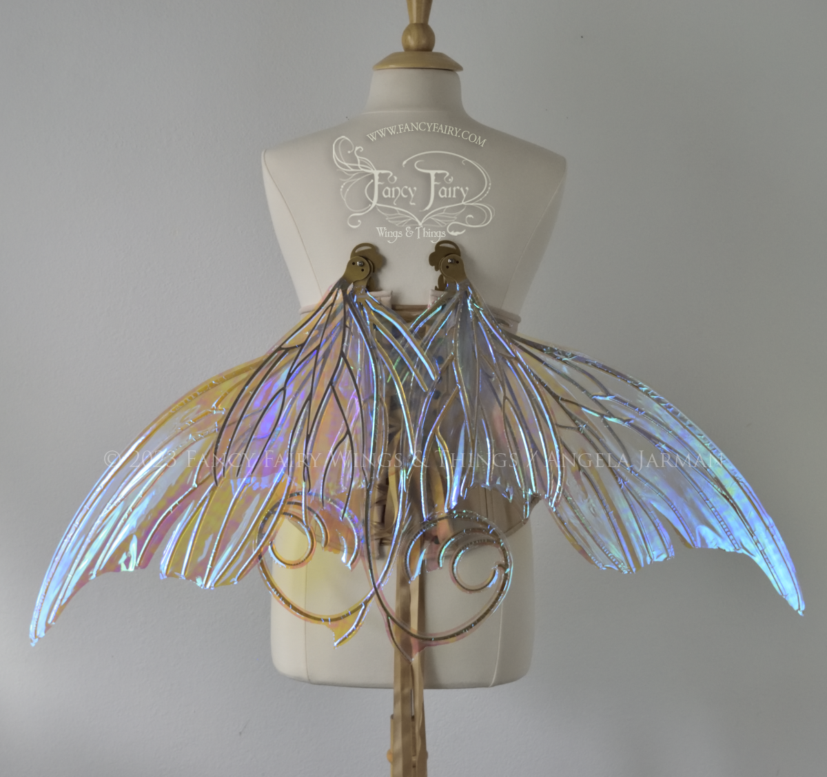 Back 3/4 view of a dress form wearing an underbust corset & large blue iridescent fairy wings with lots of intricate veins, some have 'thorns'. Upper panels curve slightly downwards along top edge with pointy tips, bottom panels have tails, wings in resting position