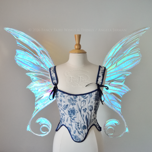 Front view of an ivory dress form wearing large transparent blue & green iridescent fairy wings with lots of intricate silver veins, some have 'thorns'. Upper panels curve slightly downwards along top edge with pointy tips, bottom panels have tails