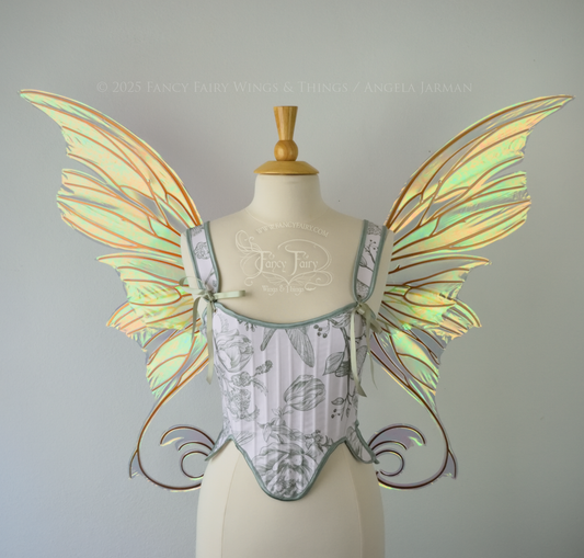 Large light green & orange iridescent fairy wings with lots of intricate veins, some with 'thorns'. The upper panels curve slightly downwards along the top edge with pointy tips, the bottom panels have tails that curve inward toward the body. Worn on a dress form which is also wearing white & sage green floral stays / bodice