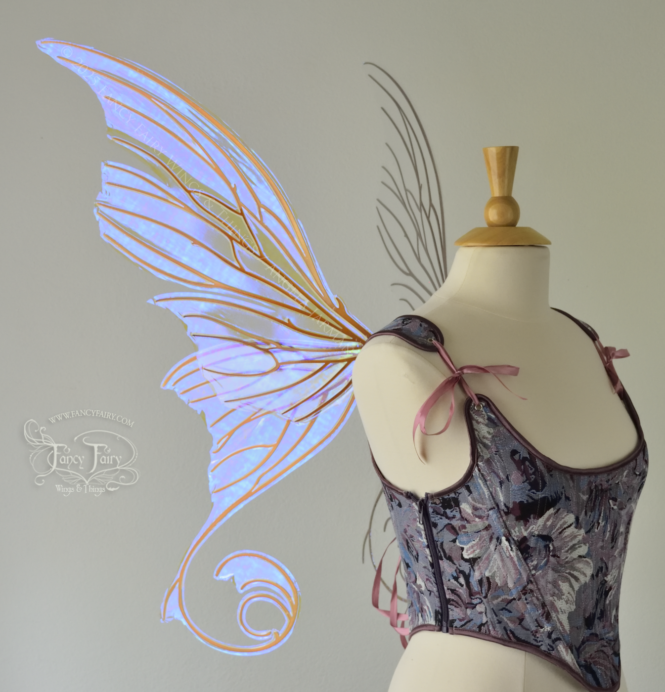 Left side view of an ivory dress form wearing large clear violet iridescent fairy wings with lots of intricate copper veins, some have 'thorns'. Upper panels curve slightly downwards along top edge with pointy tips, bottom panels have tails