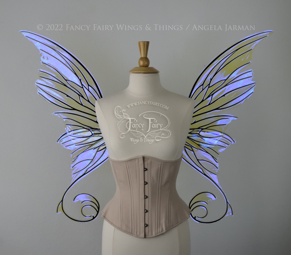 Front view of an ivory dress form wearing an alabaster underbust corset and large fairy wings with lots of intricate veins, some have 'thorns'. The upper panels curve slightly downwards along the top edge with pointy tips, the bottom panels have tails that curve inward toward the body. They are transparent and clear Ultraviolet iridescent, with black veins.