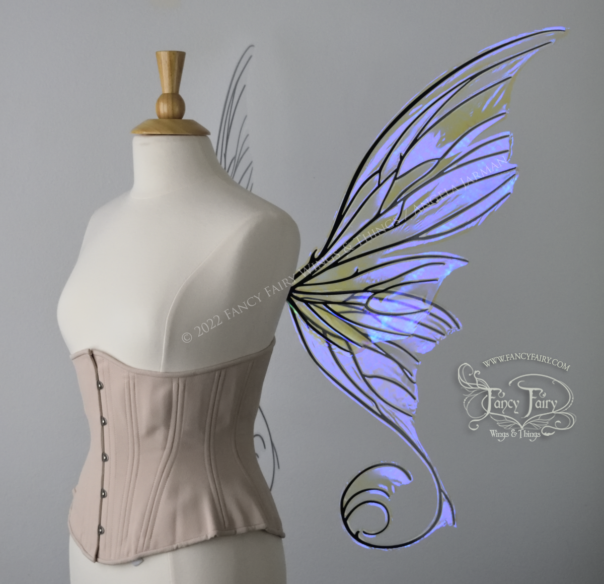 Right side view of an ivory dress form wearing an alabaster underbust corset and large fairy wings with lots of intricate veins, some have 'thorns'. The upper panels curve slightly downwards along the top edge with pointy tips, the bottom panels have tails that curve inward toward the body. They are transparent and clear Ultraviolet iridescent, with black veins.