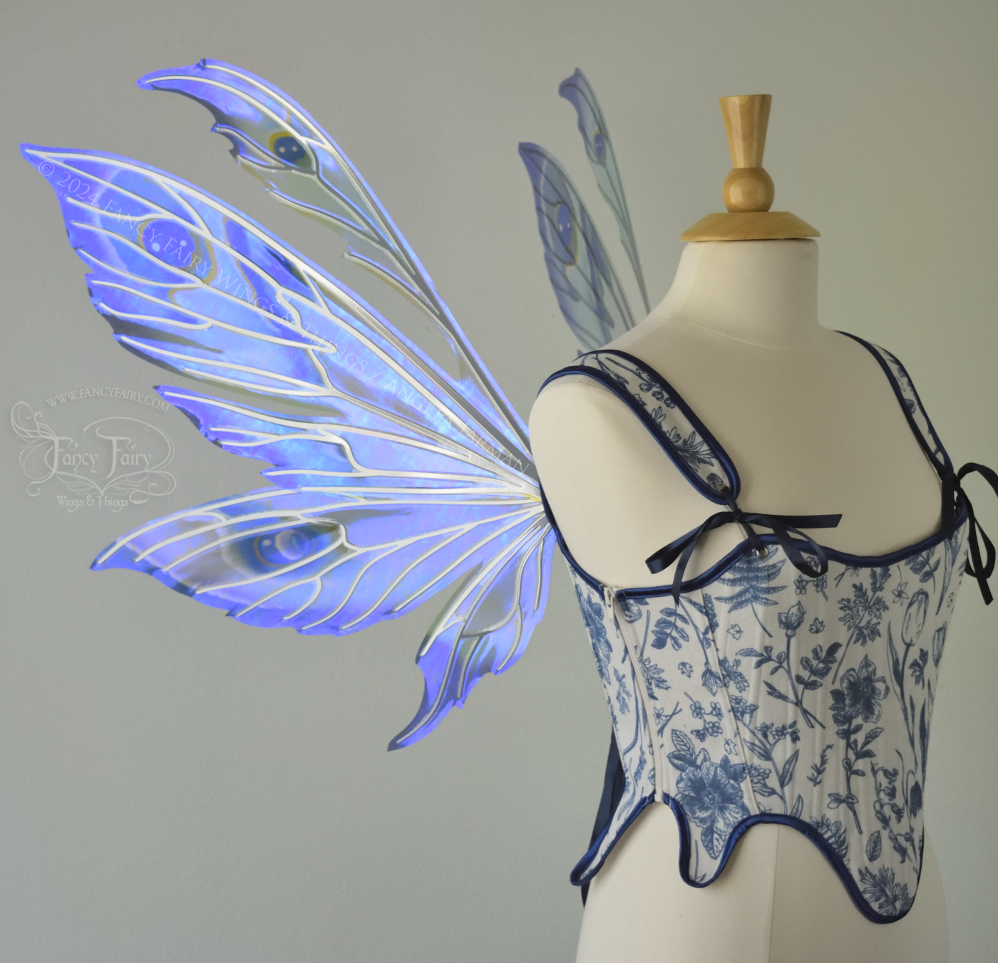 Large iridescent blue & purple painted fairy wings with pointed tips & antennae, with silver veins, worn on a dress form, left side view.