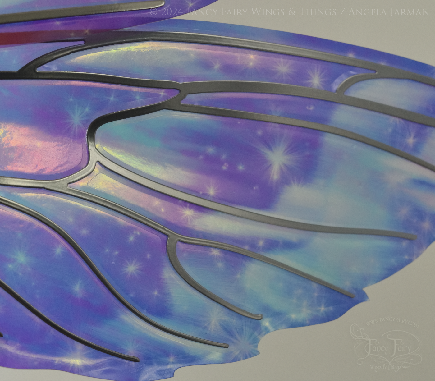 Close-up of bottom right panel of iridescent fairy wings with pointed tips & antennae, painted with auroras & stars in pinks, purples & blues, with silver veins