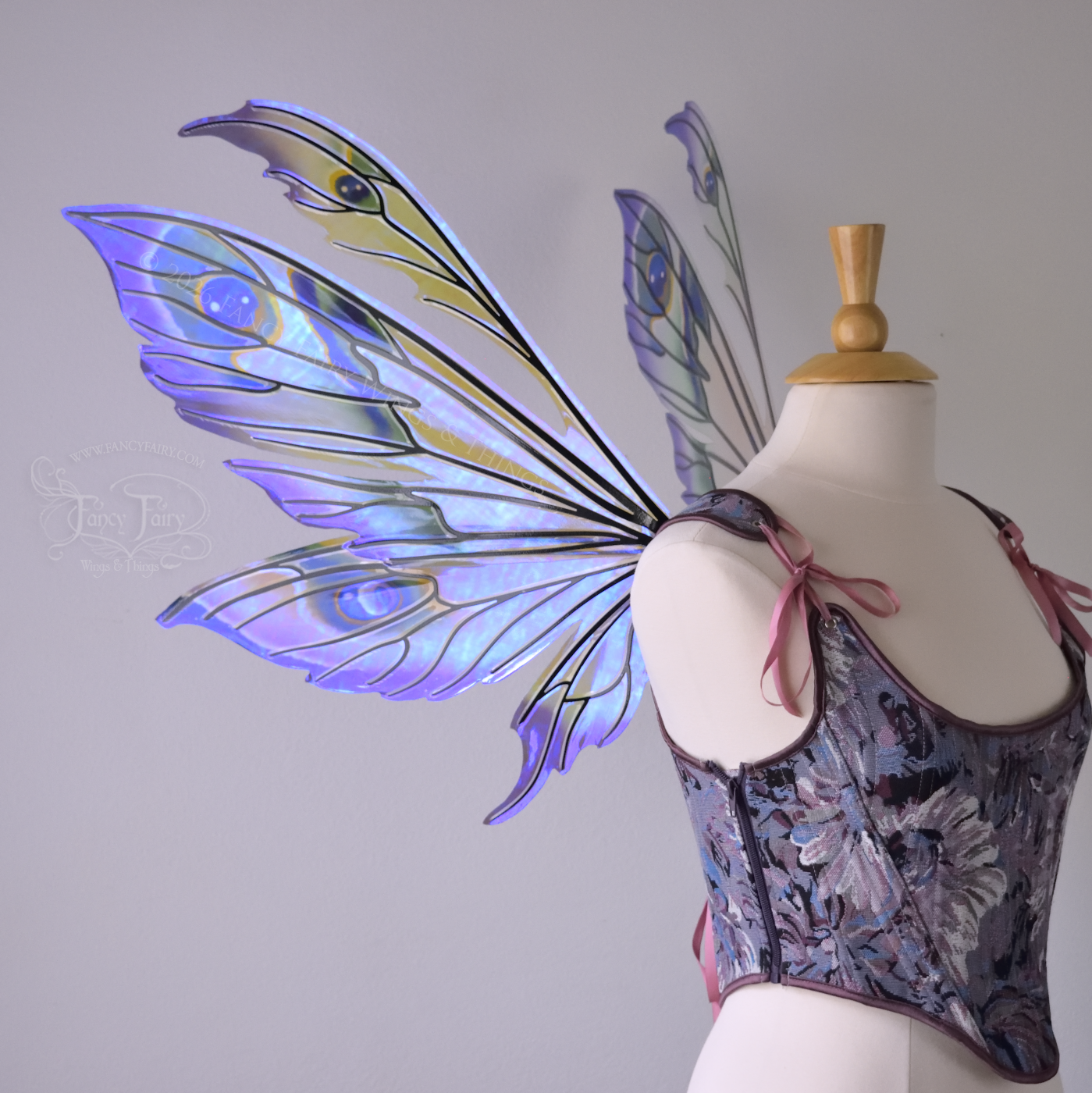 Large transparent fairy wings with antennae have peacock 'eye' accents painted on violet iridescent film with black veins, worn on dress form, left side view