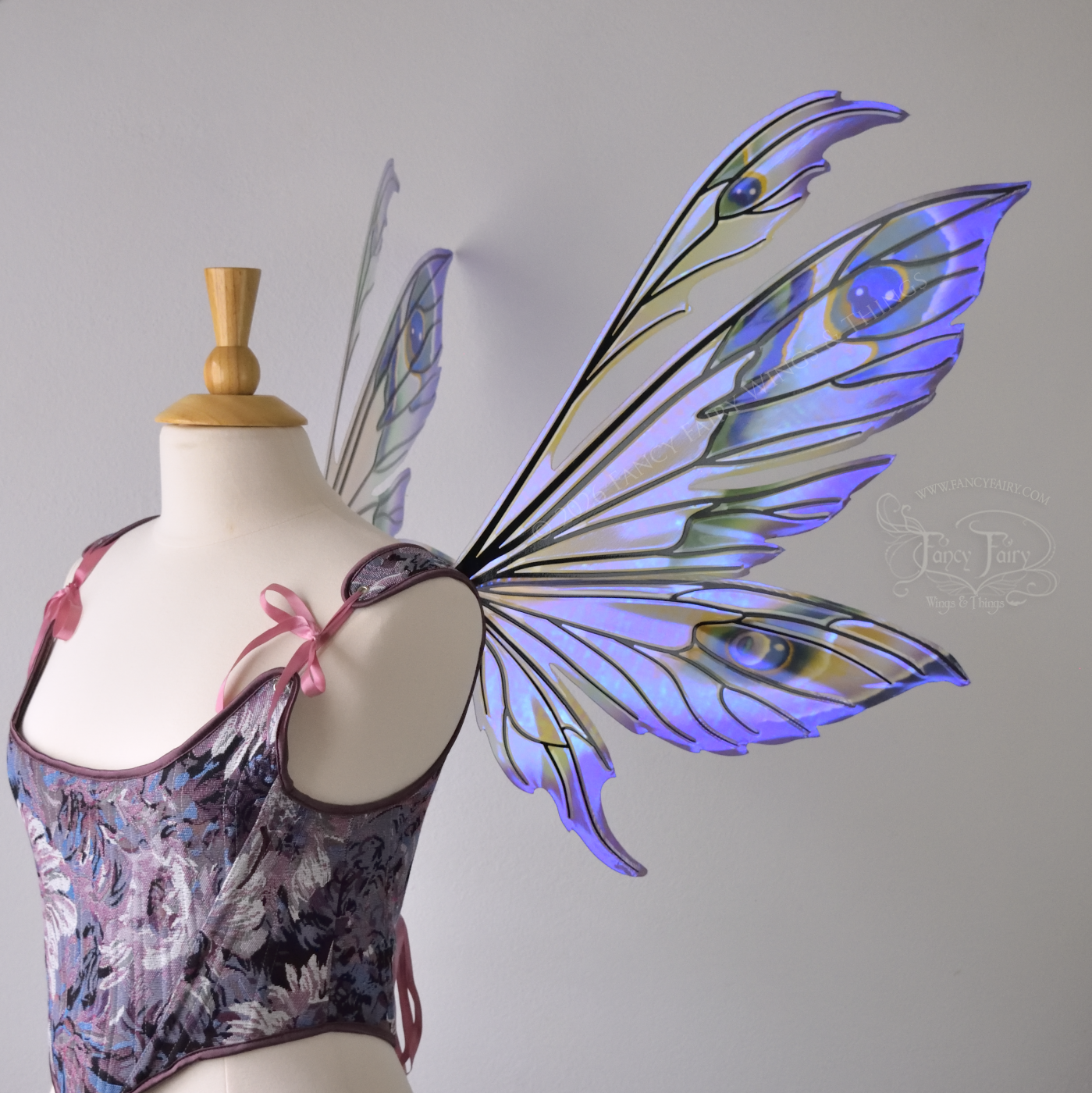 Large transparent fairy wings with antennae have peacock 'eye' accents painted on violet iridescent film with black veins, worn on dress form, right side view